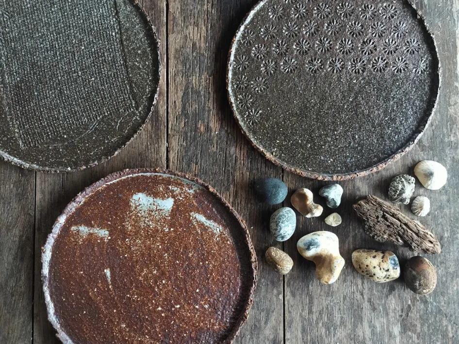 Drie handgemaakte keramische kommen met een glanzende oranje binnenzijde en decoratieve cirkelpatronen in groen- en blauwtinten aan de buitenkant.