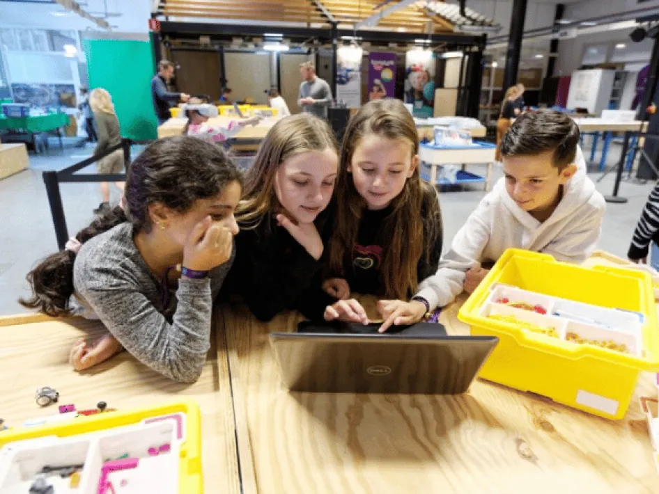 Vier Kinder, ein Junge und drei Mädchen schauen auf einen Laptop.