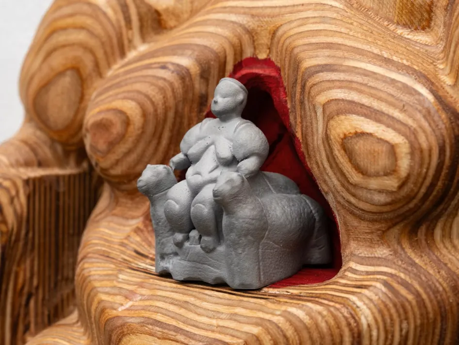 Grijs beeldje van een mythische figuur te midden van een houten sculptuur met organische lijnen, onderdeel van de tentoonstelling Fantastische Wezens.