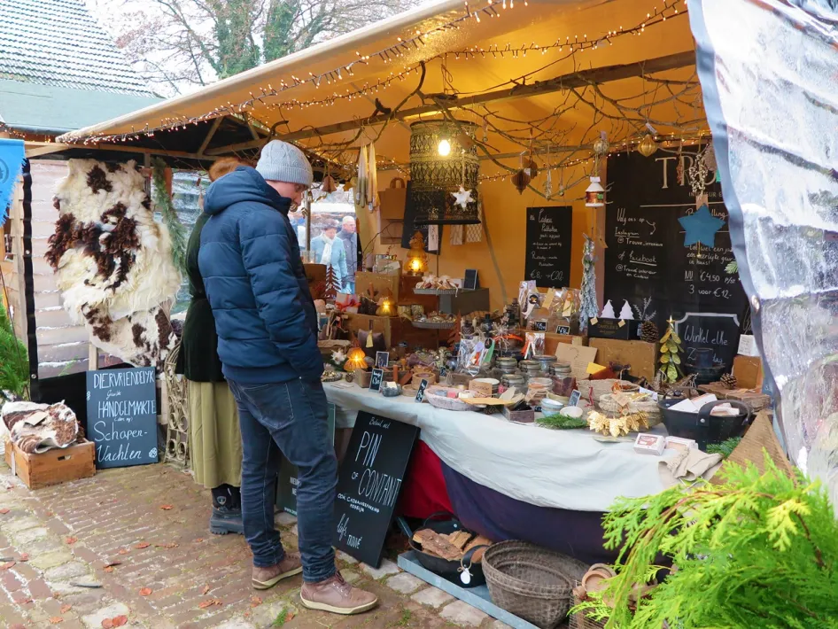 Bezoekers bekijken een sfeervolle kerstkraam met handgemaakte decoraties en cadeauartikelen.