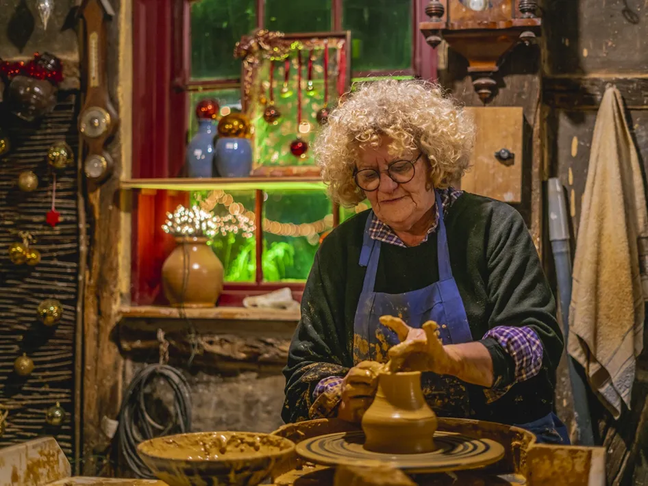 Ambachtelijke pottenbakster aan het werk in sfeervol versierde werkplaats tijdens Eynder Pieck Festeyn.