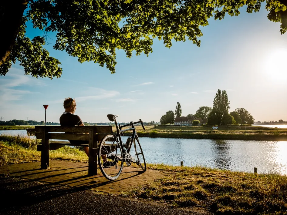 Cyclist takes a break on a bench with a view over the Maas