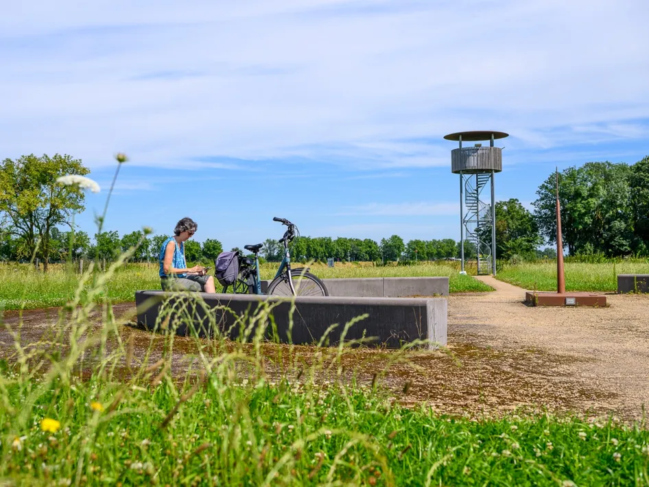 Fietser rust uit bij de uitkijktoren Walburg met uitzicht over het landschap langs de Maasstadjestour.