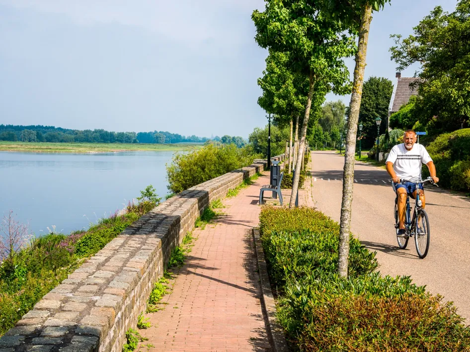 A cyclist rides along the Maas Boulevard in Asselt with views of the river during the Mother Meuse Cycle Route.