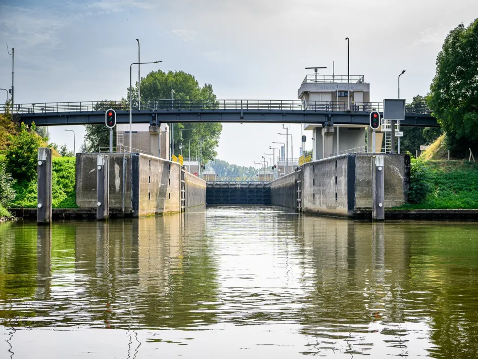 De sluis bij Osen, met het waterpeil en de betonnen sluismuren, terwijl de brug erboven verkeer en voetgangers doorlaat.