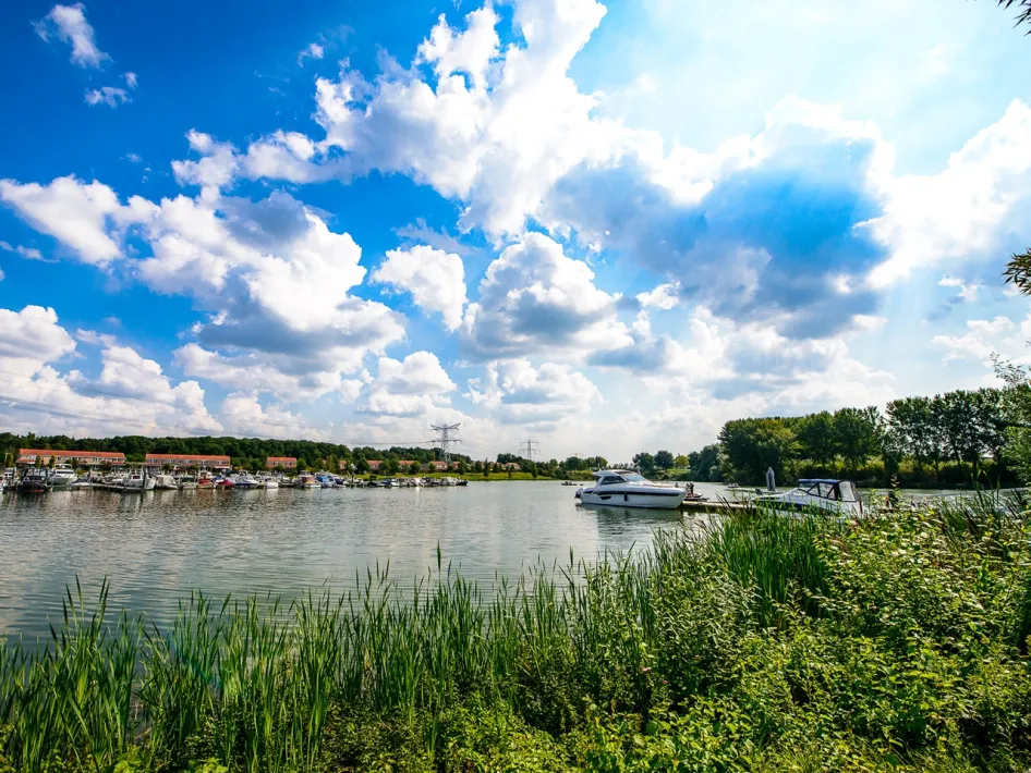 Maasplassen Circular Cycle Route along the Boschmolenplas, with boats, reeds and clouds above the water.