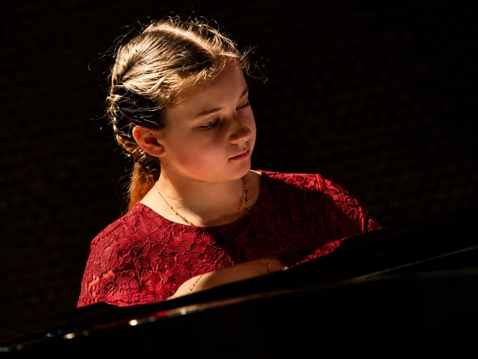 Jonge pianiste, Yulianna Beziazychna, in een rode jurk tijdens een pianoconcert, geconcentreerd achter de vleugel.