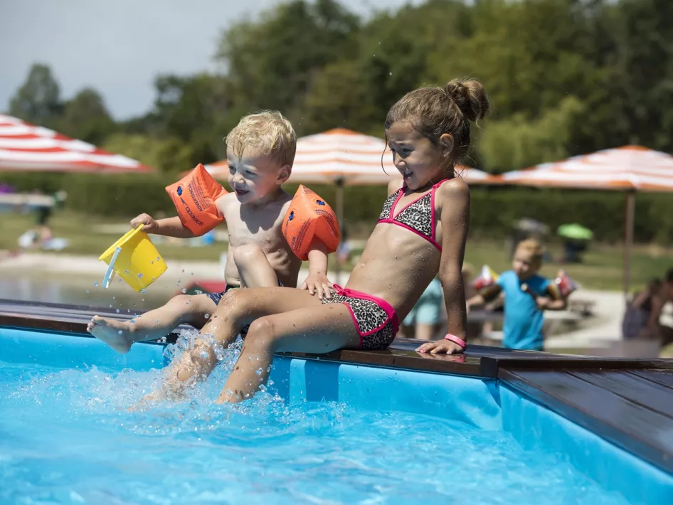 Two small children sit at the edge of the paddling pool