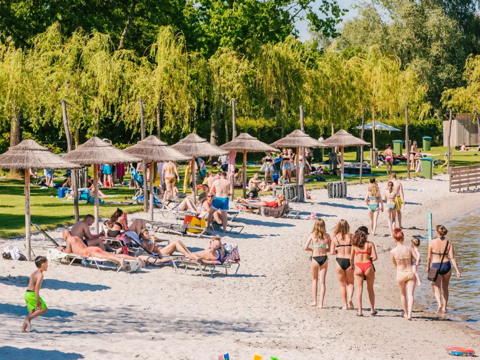 Besucher am Sandstrand am Wasser mit strohgedeckten Sonnenschirmen