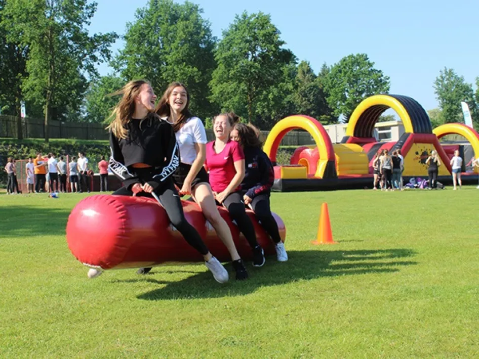 Vier jongeren doen lachend mee aan een spel op een grote rode opblaasstang bij Fun Beach - Group Events.