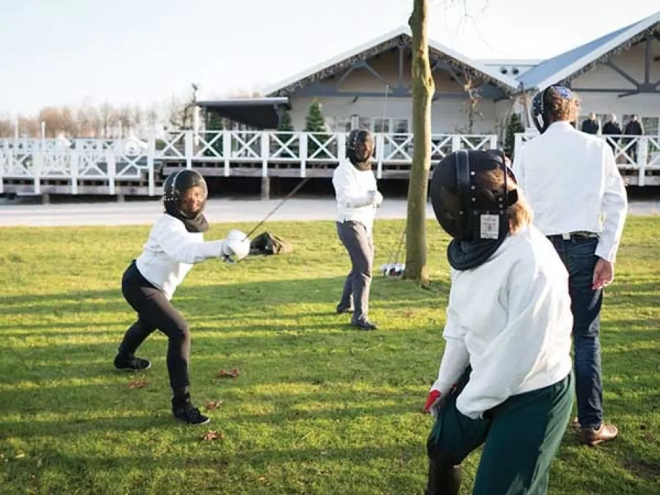 Participants practise fencing outdoors wearing protective clothing and masks at Fun Beach Group Events.