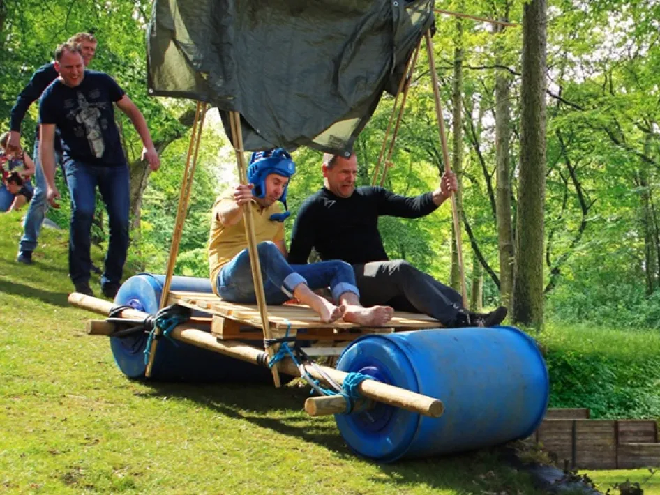 Two participants slide down a hill on barrels in a homemade wooden cart.
