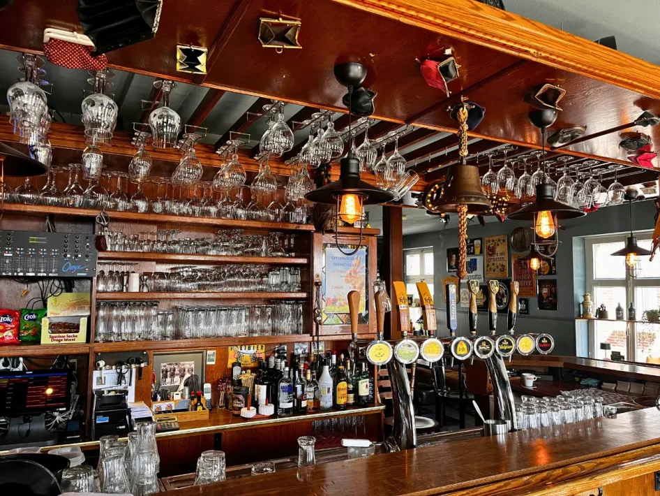 Interior of the bar at Gasterie De Knip with a wooden counter, beer taps, glasses hanging from the ceiling and warm lighting.