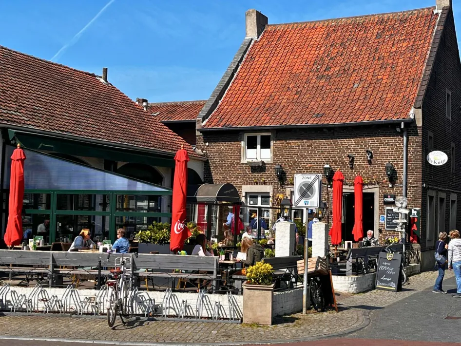 Buitenzijde van Gasterij de Knip met terras, rode parasols en historische bakstenen gevel, gelegen aan een charmant plein.