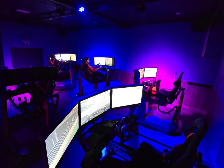 Sfeervolle racezaal bij Gearbox Race Café, verlicht in blauw en paars, met meerdere racesimulatoren in actie.