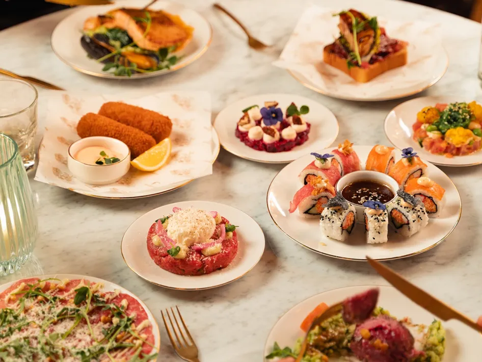 Ein Tisch voller bunter und abwechslungsreicher Gerichte, darunter Sushi, Kroketten und Tartar, die ansprechend präsentiert werden.