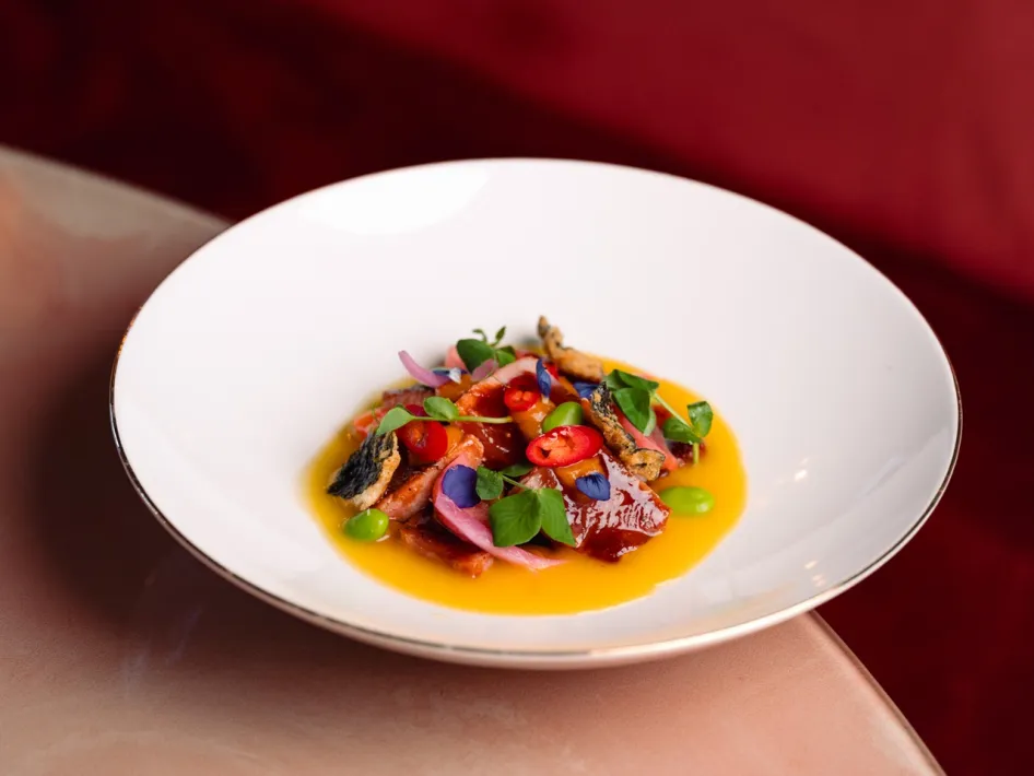 Culinary appetiser with colourful ingredients, served in a white bowl on a pink marble table.