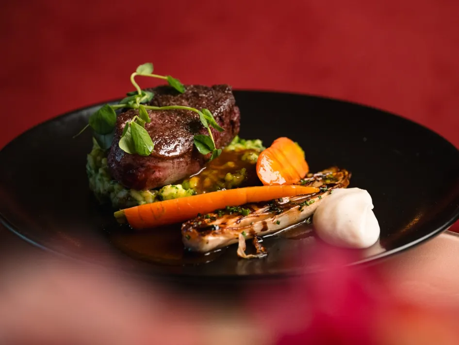 Leckeres Hauptgericht mit zartem Fleisch, Gemüse der Saison und Soße, serviert auf einer schwarzen Platte.