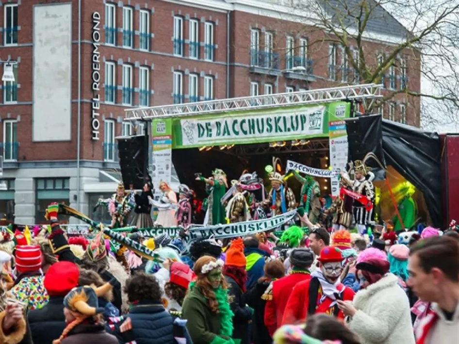 Feestelijke sfeer op Greune Maondaag in Roermond – Carnavalsvierders genieten van livemuziek en optredens op het Bacchusklap-podium op het Stationsplein.