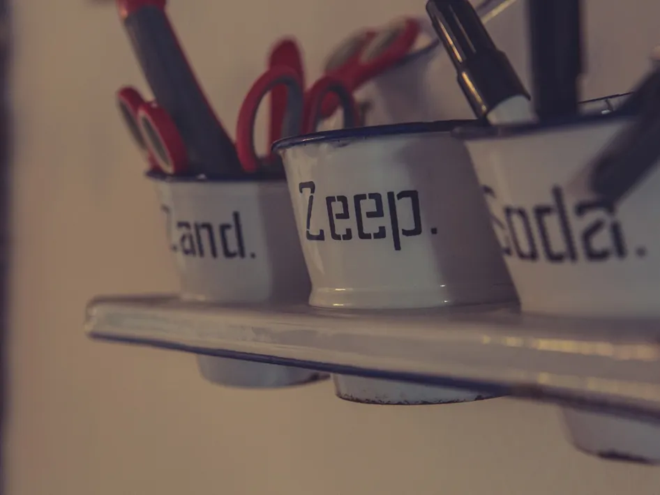 Close-up van metalen potjes met opschrift op een plank, gevuld met scharen en pennen.