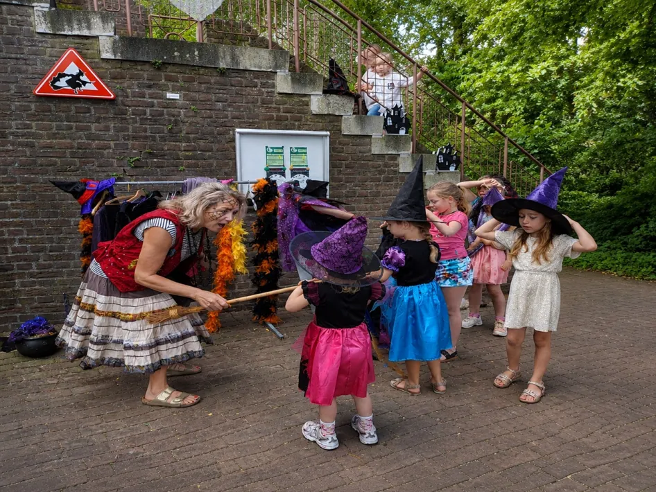 Kinderen verkleed als heksen nemen samen met een heks deel aan een speelse heksenactiviteit met bezemstelen bij de Rattentoren in Roermond.