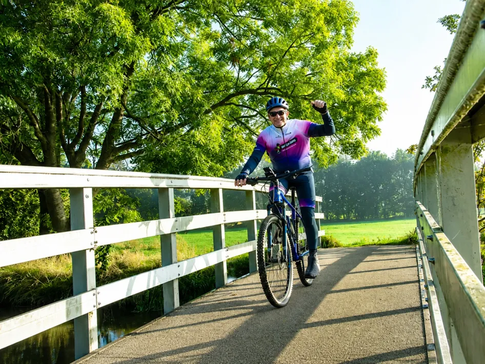 Deelnemer aan de Heksenheuveltocht fietst over een brug in het groene landschap van Nederweert tijdens de mountainbike- en graveltocht.
