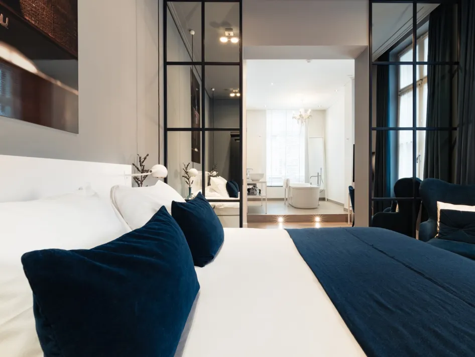 Hotelkamer Cipier in Het Arresthuis in Roermond, met wit beddengoed, donkerblauwe accenten en een vrijstaand bad.