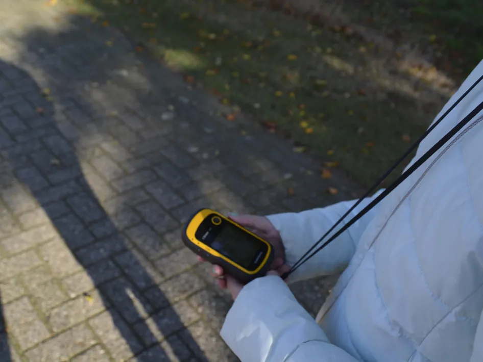 Person holding a GPS device during a GPS based game on a forest path