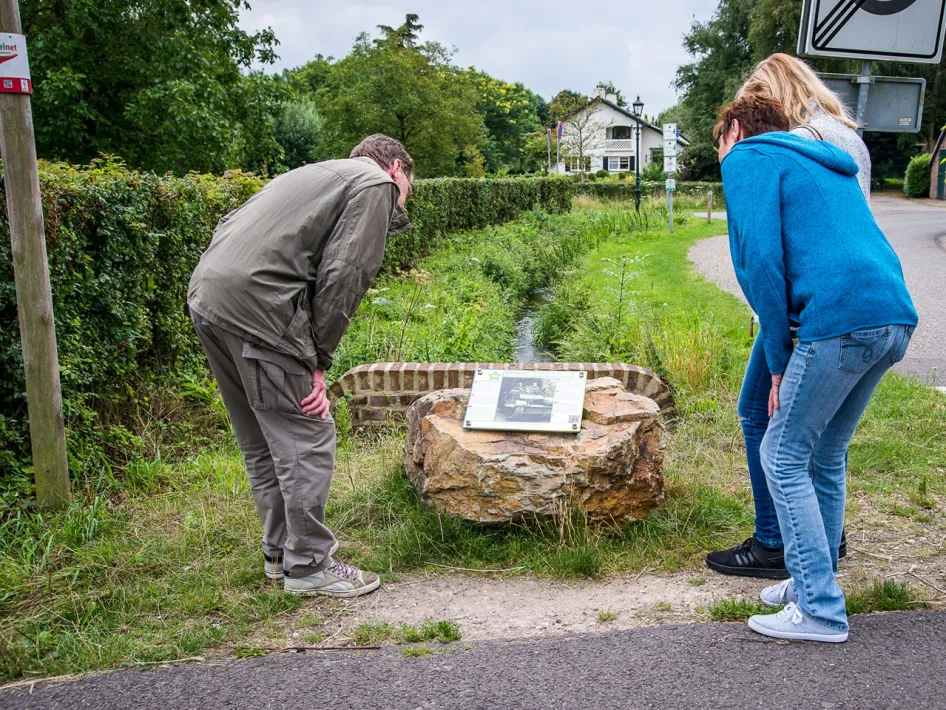 Three hikers bend over an information board at a Liberation Route Europe audio spot, a historic point along the Hiking Trail Limburg.