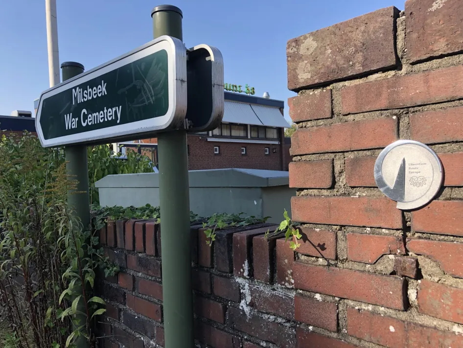 Een metalen Vector of Memory van de Liberation Route Hiking Trail Europe bij het Milsbeek War Cemetery, een belangrijke herdenkingsplek langs de Hiking Trail Limburg.