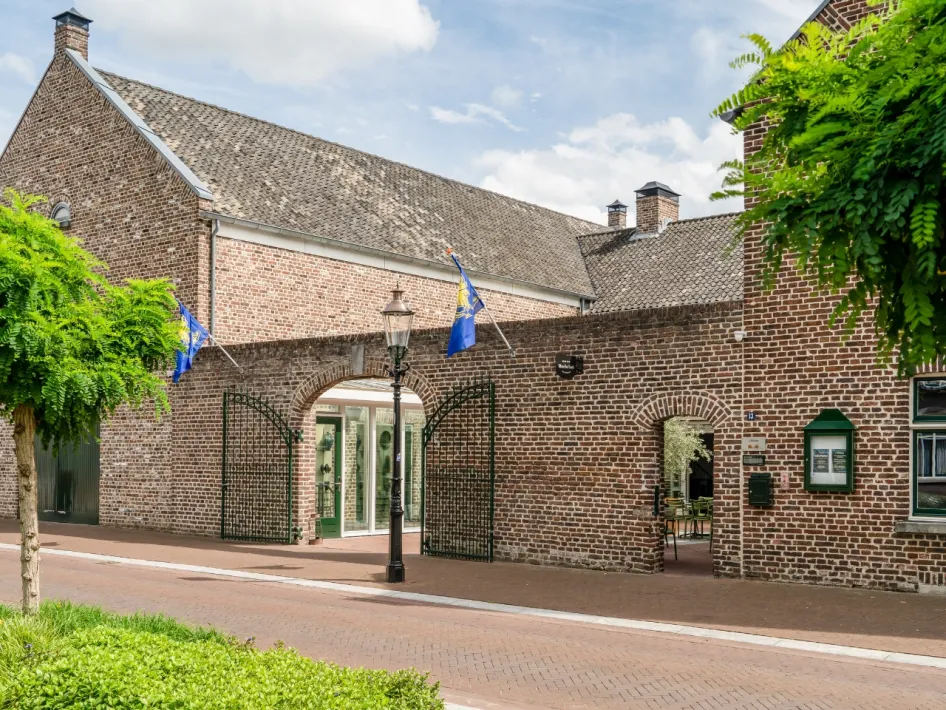 Authentieke bakstenen gevel van Hoeve de Bongerd met groene deuren en poort, gelegen aan een rustige straat in Beesel.