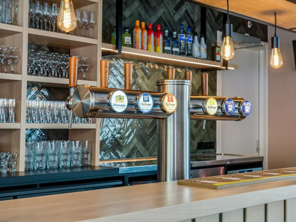 Nahaufnahme einer Zapfanlage mit verschiedenen Bieren und Gläsern im Hintergrund in einer schick gestalteten Bar.