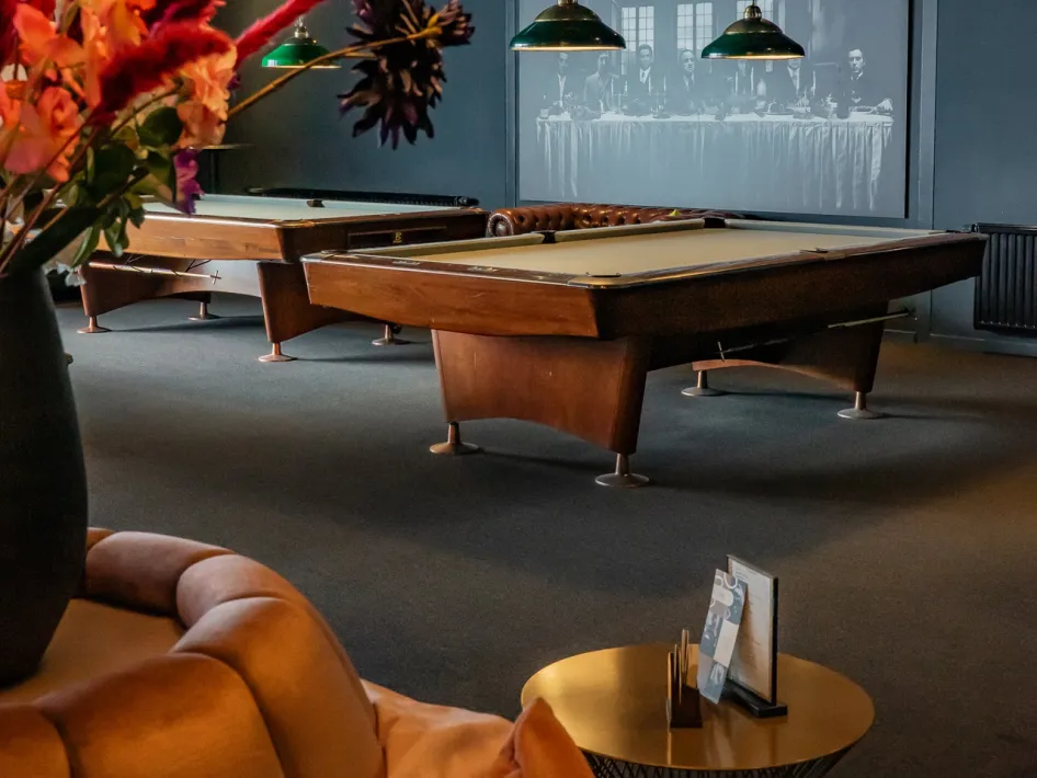 Eine Reihe klassischer Pooltische steht in der Hornerhof Pool- & Snooker Bar, mit grünen Lampen über den Tischen.