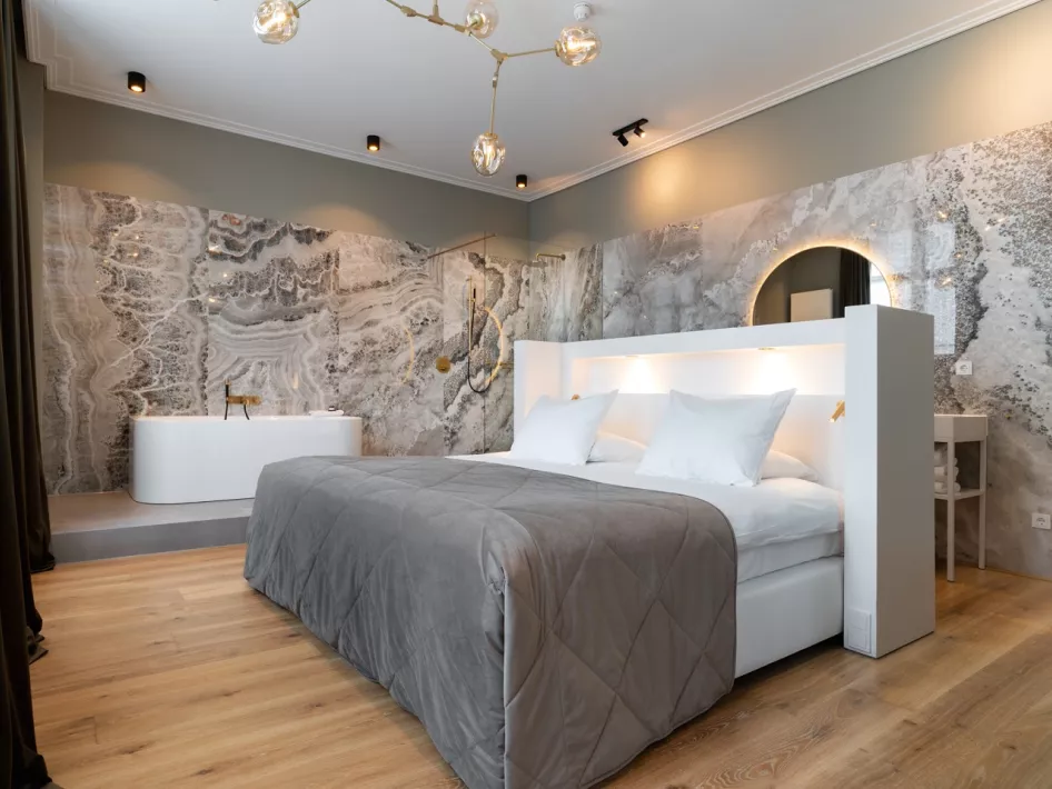 Luxe hotelkamer in Het Arresthuis in Roermond, met een comfortabel tweepersoonsbed, modern interieur, een stijlvolle marmeren wand en een vrijstaand ligbad.