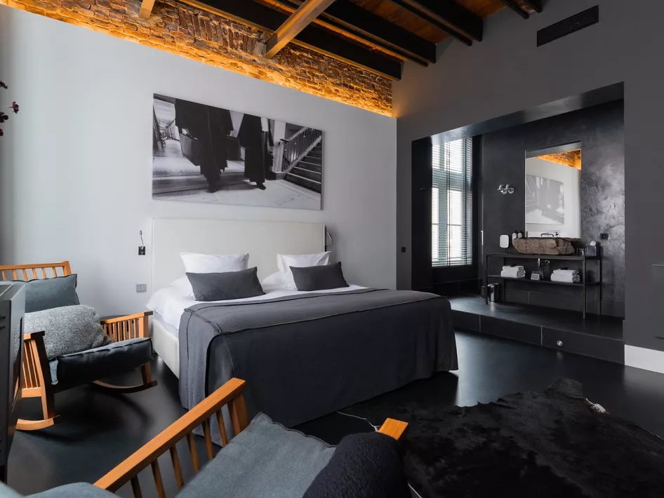 Luxuriöses Hotelzimmer im Het Arresthuis in Roermond mit einem bequemen Doppelbett, moderner Einrichtung, einer stilvollen Marmorwand und einer freistehenden Badewanne.