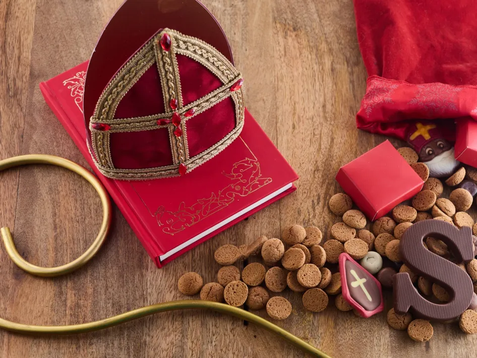 Op een houten tafel liggen een rode mijter, een staf, een rood boek, kruidnoten, chocoladeletters en cadeautjes naast een opengebroken jutezak in het Huis van Nicolaas in Weert.
