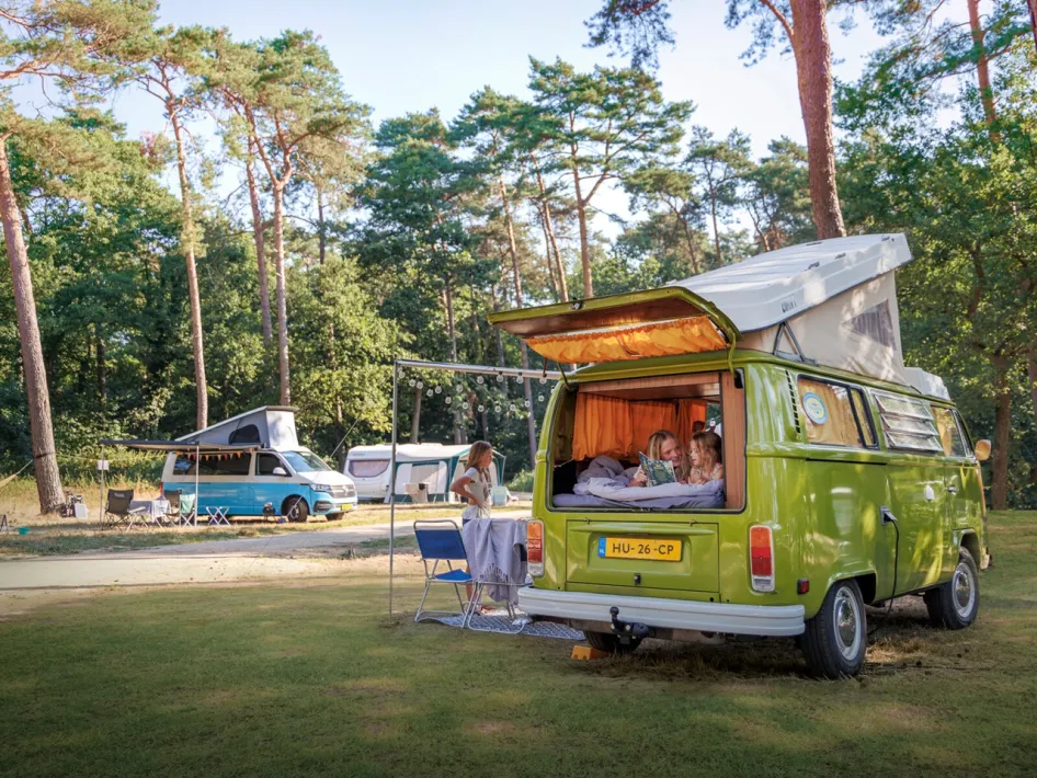Familie campt mit einem Retro-Campingbus und Zelten auf einer großen Wiese im Wald