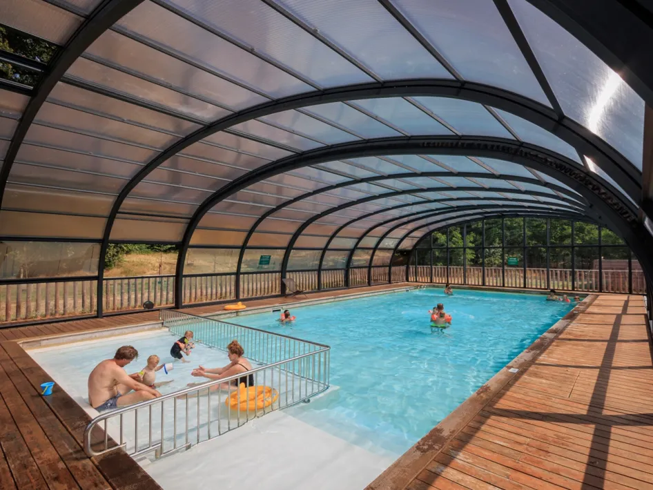 Überdachtes Schwimmbad mit Familien und Kindern im Wasser an einem sonnigen Tag