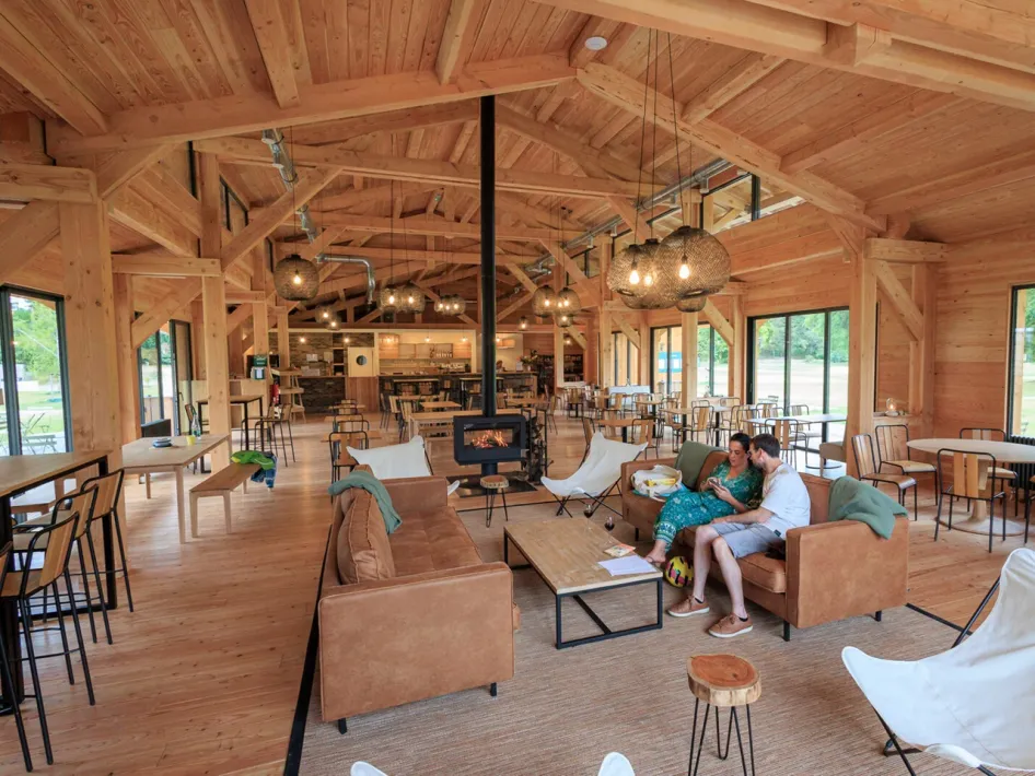 Houten recreatieruimte met zithoeken, open haard en mensen die ontspannen op de bank