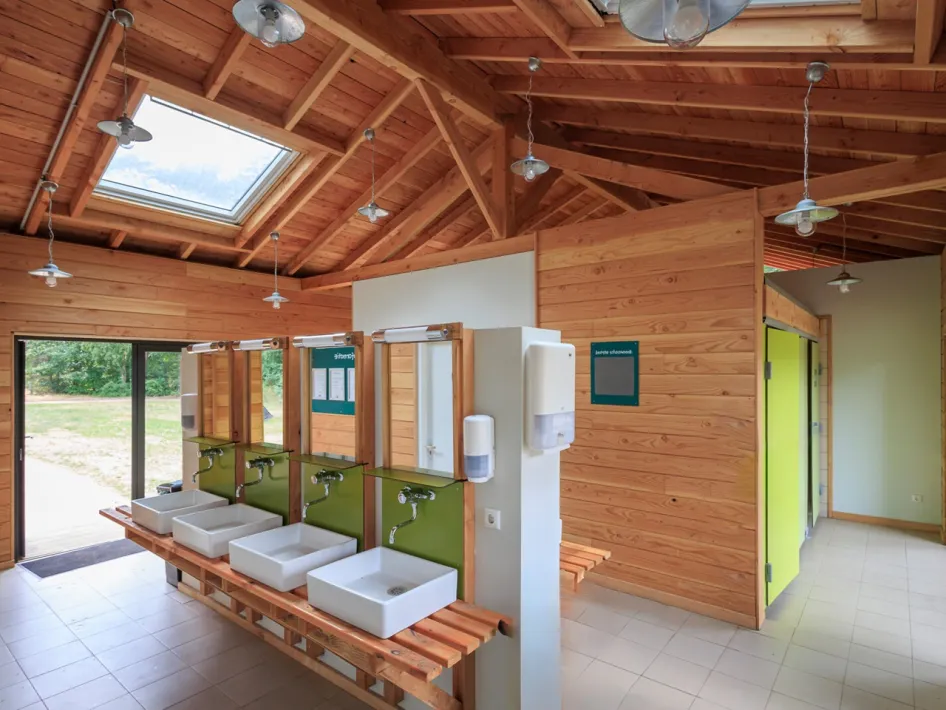 Modern sanitairgebouw met houten afwerking, wasbakken en douches op de camping