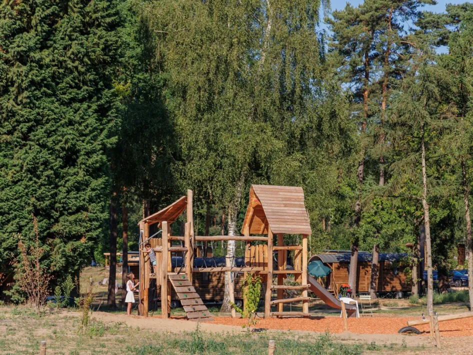 Houten speeltuin met glijbaan en klimtoren op een open plek tussen de bomen