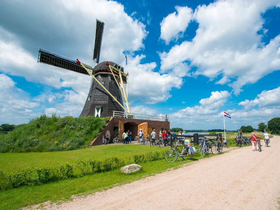 Zicht op moBlick auf die Mühle De Grauwe Beer in Beesel, mit Radfahrern und Wanderern am Eingang unter blauem Himmel.len De Grauwe Beer in Beesel met fietsers en wandelaars bij de ingang onder een blauwe lucht.