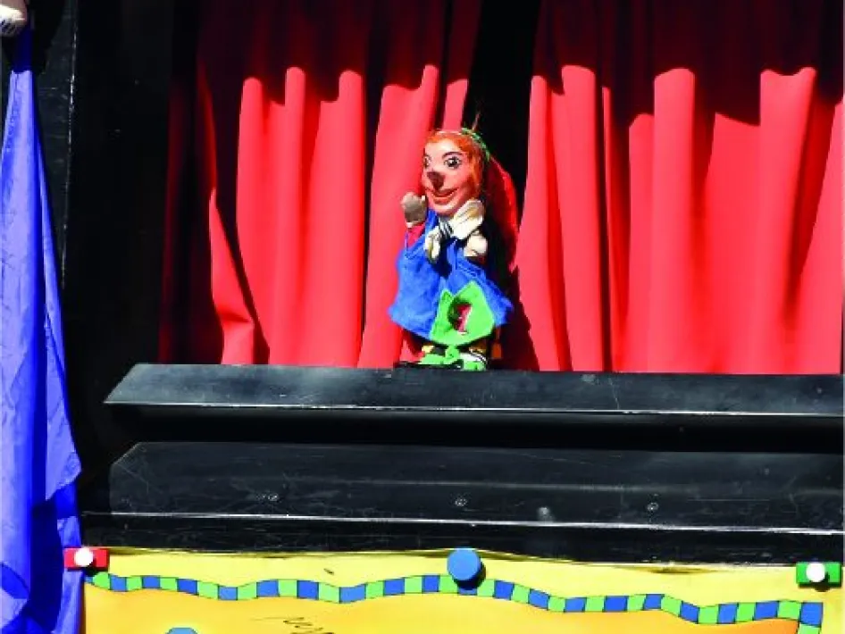 Poppenkast met een personage uit de poppenkastvoorstelling van Jan Klaassen op het podium, voor een rood gordijn