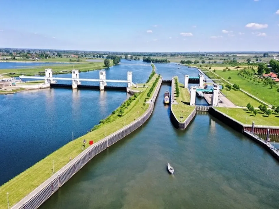 Luchtfoto van een stuw- en sluiscomplex in de Maas, met meerdere sluiskolken, passerende schepen en groene oevers in het open landschap van Midden-Limburg.