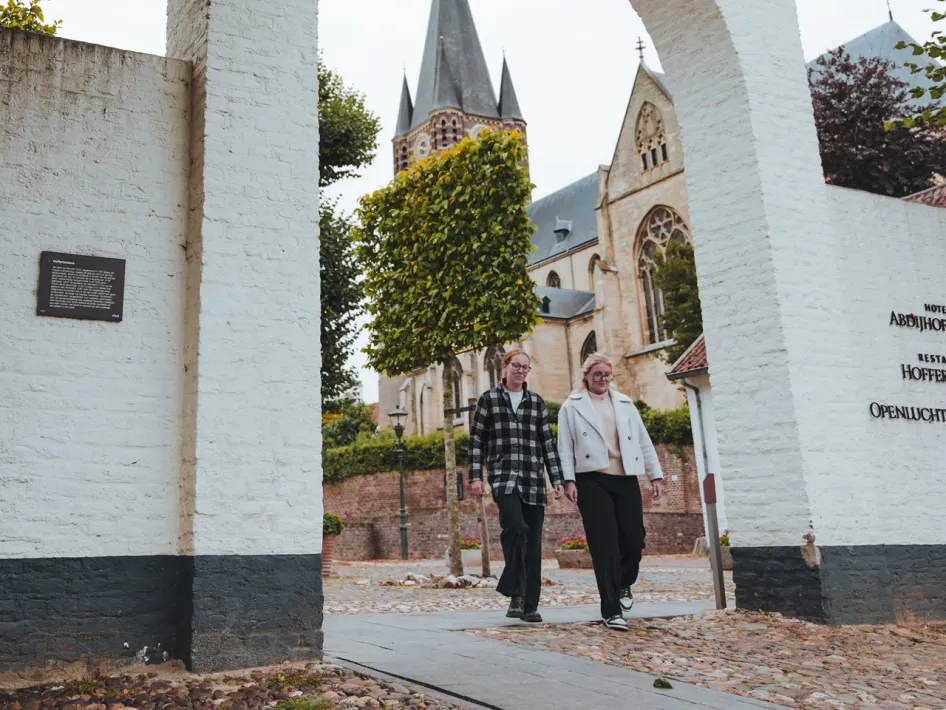 Zwei Wanderer gehen durch das historische Stadttor von Thorn, mit der Abteikirche im Hintergrund.