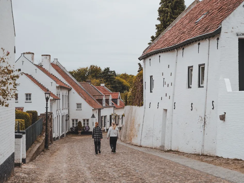 Zwei Wanderer gehen durch eine stimmungsvolle Straße mit weißen Häusern im historischen Zentrum von Thorn.