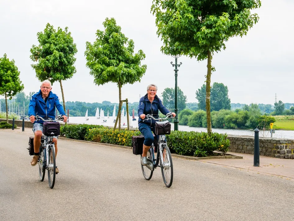 Two cyclists ride along the water on the International Meuse Cycle Route in Asselt.