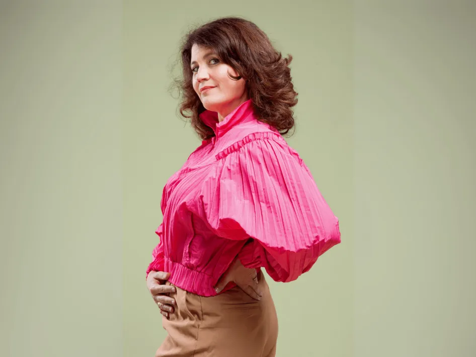 Julika Marijn in een puffy, roze blouse. Ze staat met haar linkerkant richting de camera, haar rechterhand op haar buik en de ander op haar heup leunend.