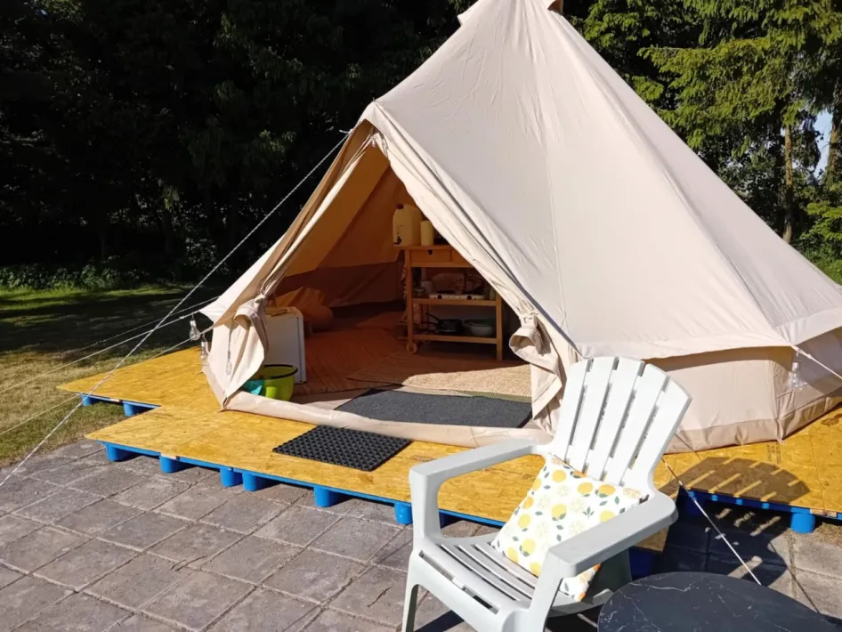 Spacious bell tent with wooden decking, interior furnishings, and outdoor seating area at Kampeerderij De Kaaiewaaier.