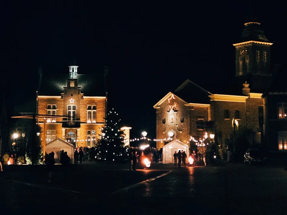 Een plein in Stevensweert met een grote kerstboom, verlichte gevels, vuurkorven en bezoekers die samen het Kaarsenfeest Stevensweert vieren.